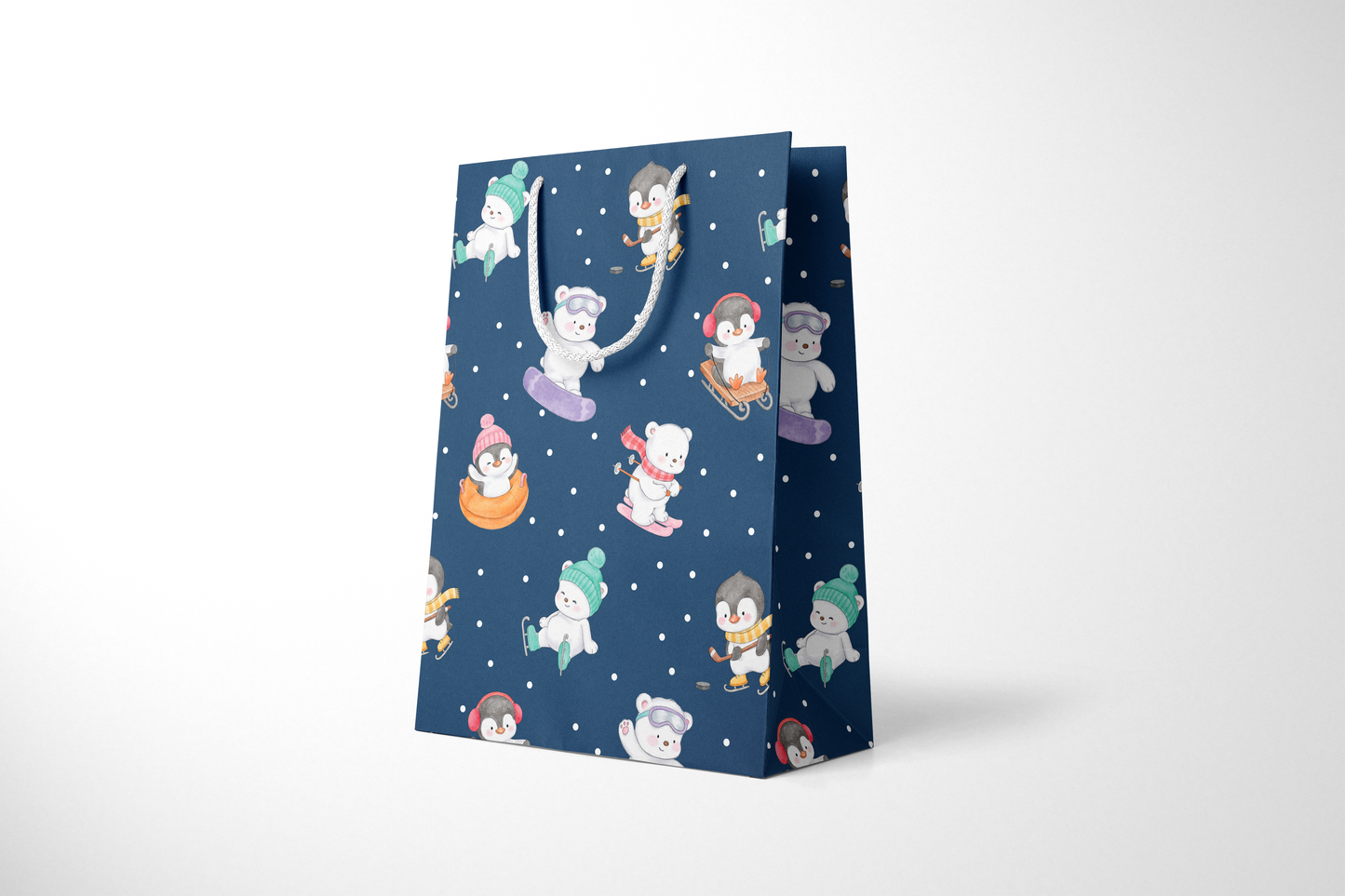 Side view of a navy blue gift bag with playful illustrations of polar bears and penguins enjoying winter activities like snowboarding, sledding, tubing, skating, and hockey, accented with white snow dots and white rope handles.