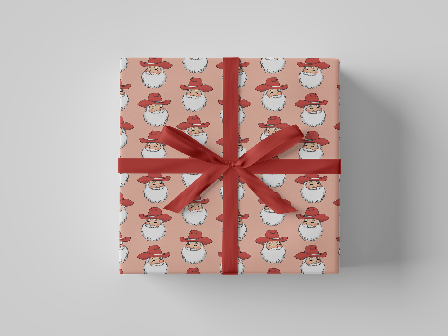 Front view of smiling Cowboy Santa Claus in a red cowboy hat, featured on peach-colored Christmas wrapping paper