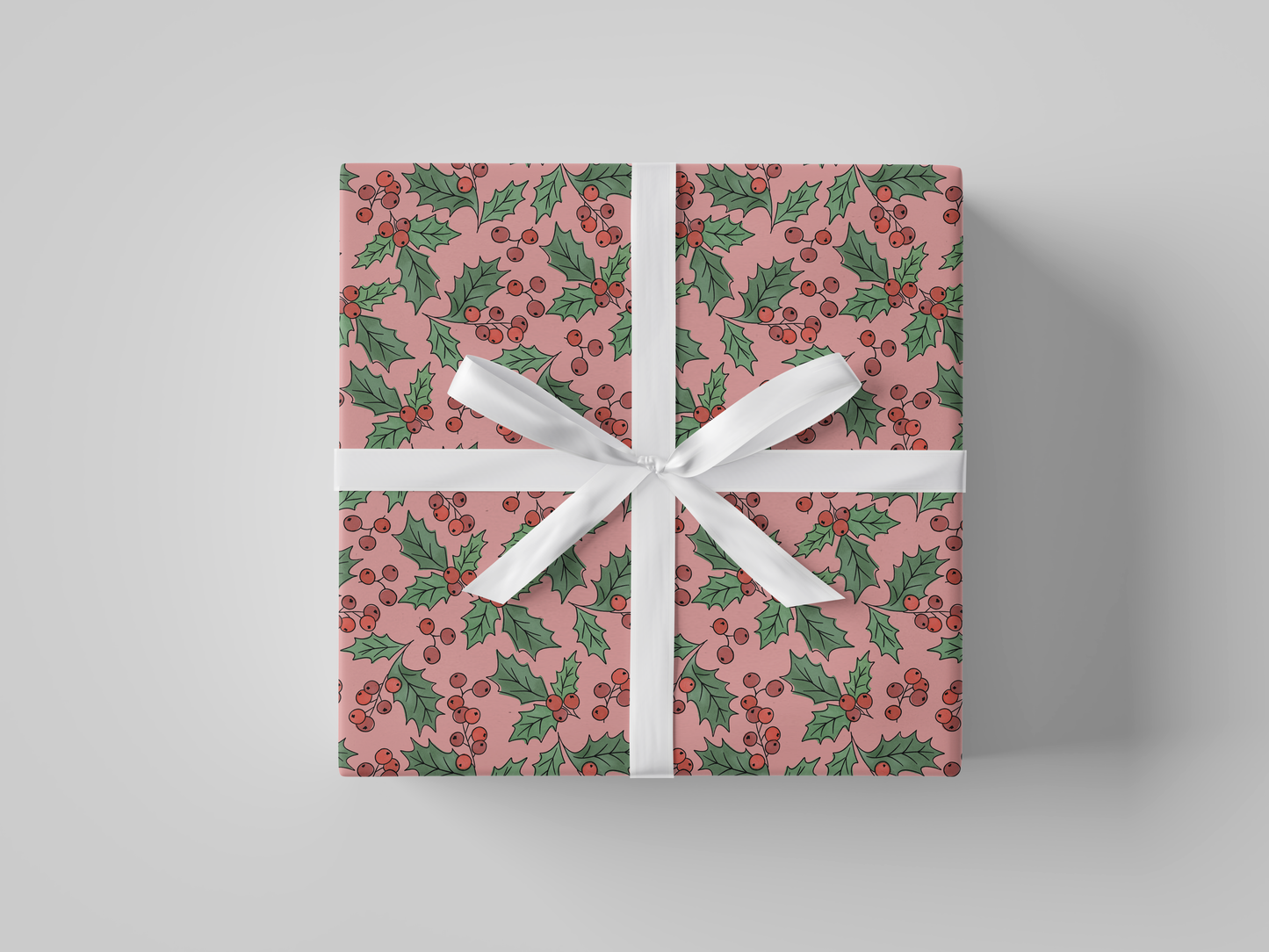 Front view of light pink-colored wrapping paper adorned with Christmas holly, showcasing red berries and green leaves.