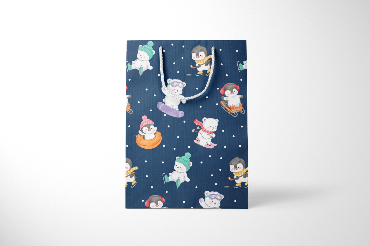 Front view of a navy blue gift bag with playful illustrations of polar bears and penguins enjoying winter activities like snowboarding, sledding, tubing, skating, and hockey, accented with white snow dots and white rope handles.