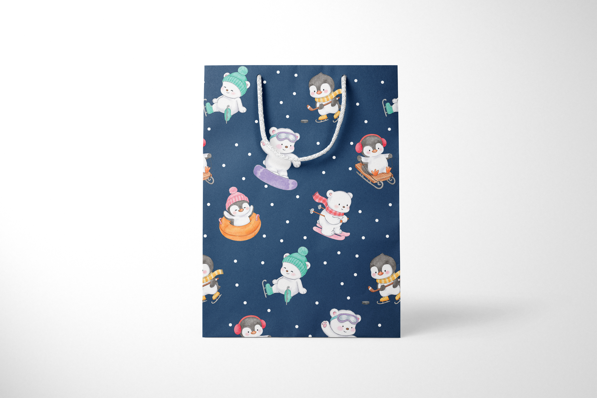 Front view of a navy blue gift bag with playful illustrations of polar bears and penguins enjoying winter activities like snowboarding, sledding, tubing, skating, and hockey, accented with white snow dots and white rope handles.