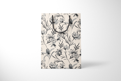 Front view of cream gift bag with hand-drawn black and gray floral illustrations, finished with black rope handles.