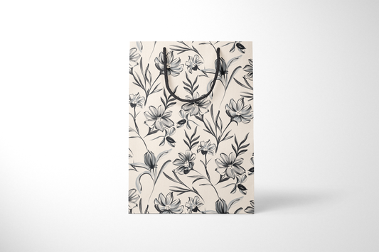 Front view of cream gift bag with hand-drawn black and gray floral illustrations, finished with black rope handles.