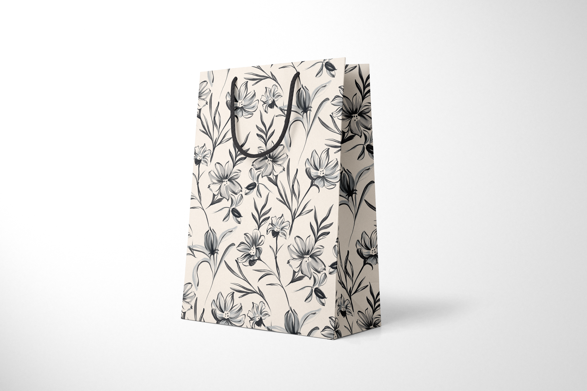 Side view of cream gift bag with hand-drawn black and gray floral illustrations, finished with black rope handles.