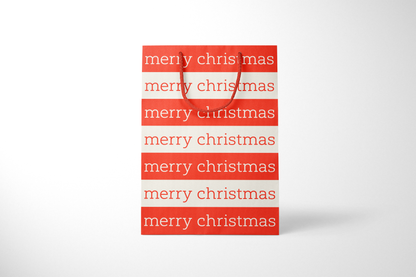 Front view of modern minimalist gift bag featuring alternating red and cream stripes with repeating ‘merry christmas’ text in bold typography, finished with sturdy red rope handles.