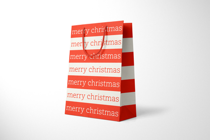 Side view of modern minimalist gift bag featuring alternating red and cream stripes with repeating ‘merry christmas’ text in bold typography, finished with sturdy red rope handles.
