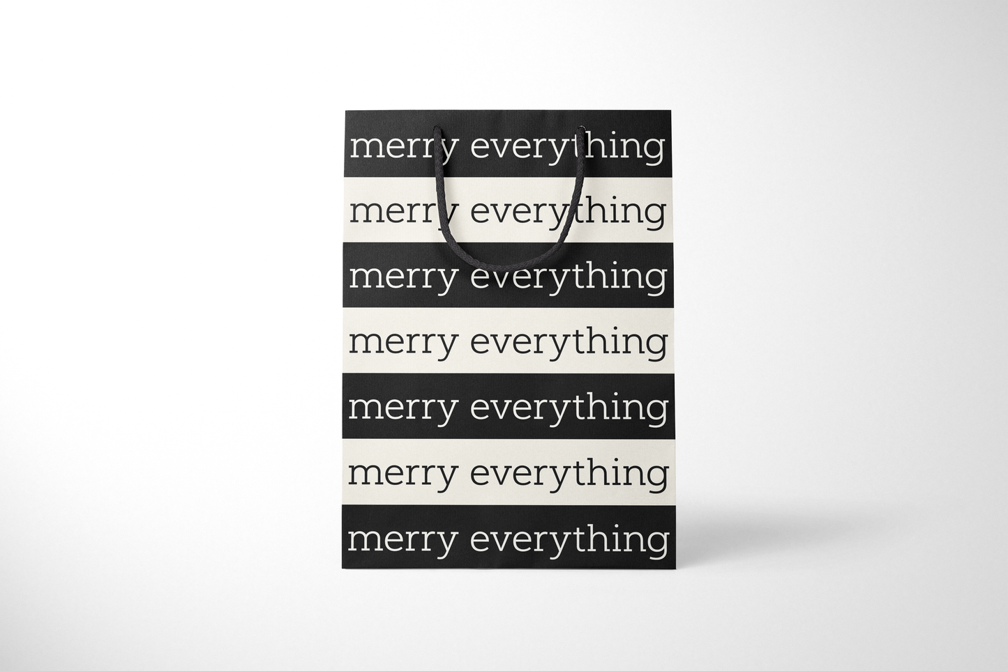 Front view of modern minimalist gift bag featuring alternating black and cream stripes with repeating ‘merry everything’ text in bold typography, finished with sturdy black rope handles.