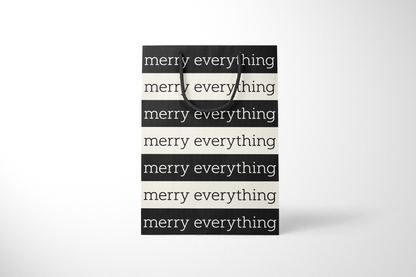 Front view of modern minimalist gift bag featuring alternating black and cream stripes with repeating ‘merry everything’ text in bold typography, finished with sturdy black rope handles.
