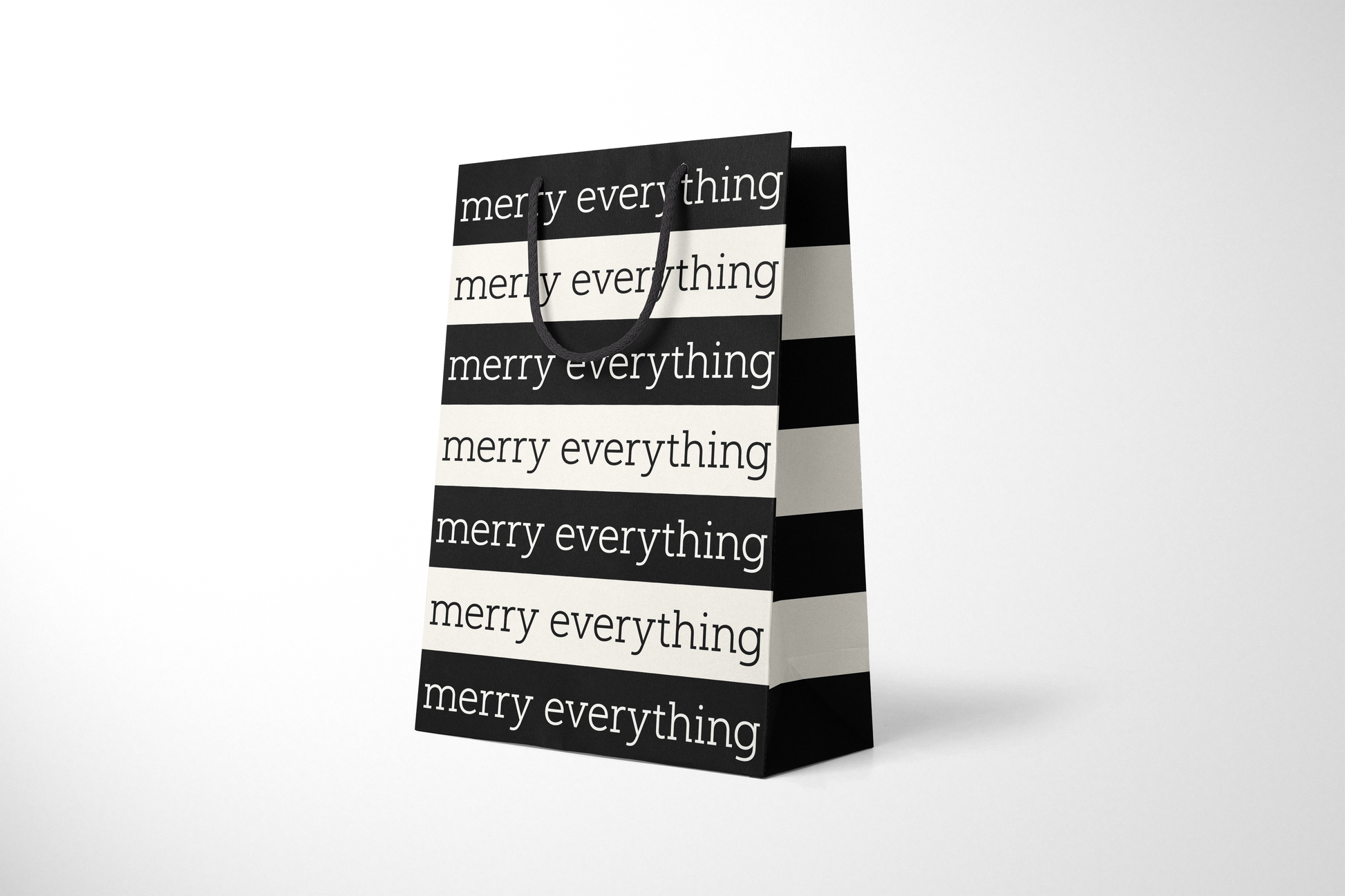 Side view of modern minimalist gift bag featuring alternating black and cream stripes with repeating ‘merry everything’ text in bold typography, finished with sturdy black rope handles.
