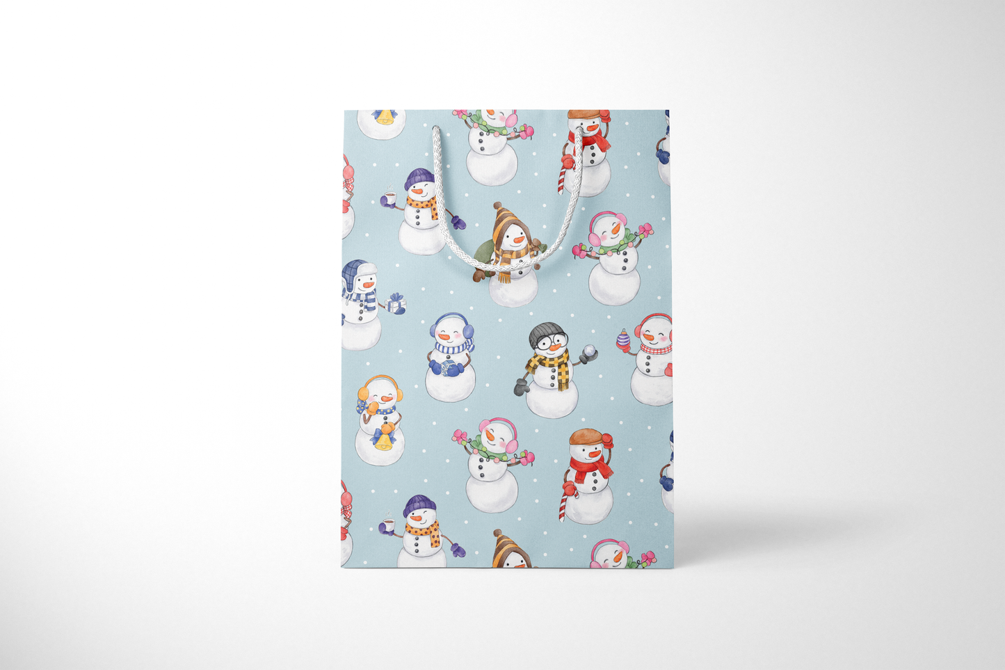 Front view of light blue gift bag with a whimsical snowman pattern, featuring snowmen in colorful scarves, hats, and earmuffs, holding holiday items like gifts, candy canes, and hot cocoa, with white rope handles and scattered snow dots and a white rope handles.