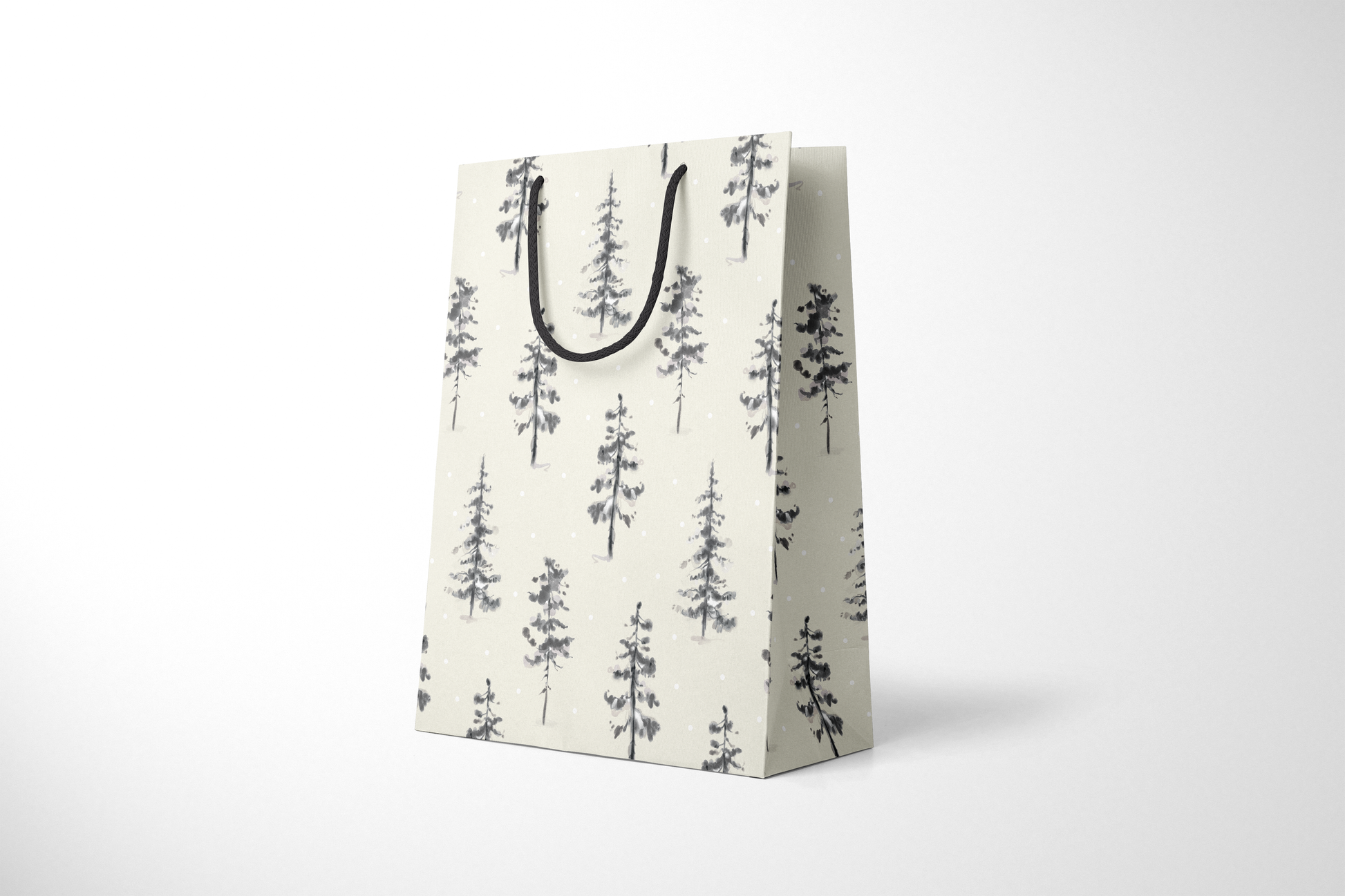 Side view of cream-colored holiday gift bag with hand-painted black and gray evergreen trees scattered across the surface, accented with falling snow dots, and finished with black rope handles.